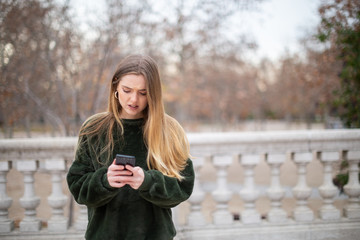 Worried woman looking at smartphone in park