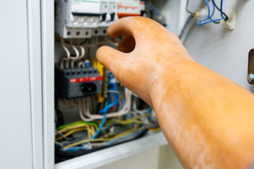 the hand of a man in a dielectric glove with a screwdriver moves towards the switchboard