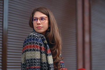 Thoughtful woman wearing glasses and a tweed coat on brown urban