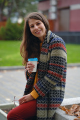  young woman in coat drinking coffee outdoors.