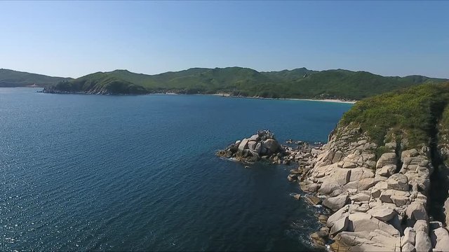Aerial shot moving along the coastline of deep blue sea along a dramatic cliff edge on sunny day