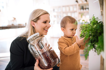A young woman with a toddler boy buying groceries in zero waste shop.
