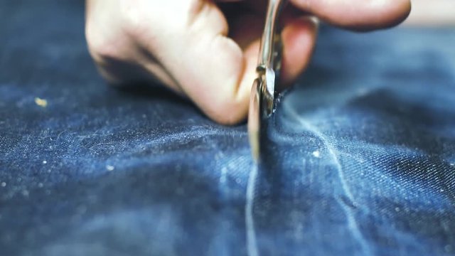 Hand of Seamstress cutting a Jeans fabric with scissors on wooden table 