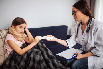 Sick small girl take white tissue from doctor's hands. She look at them and hold one hand on head. Nice young woman look at patient. She sit beside her.