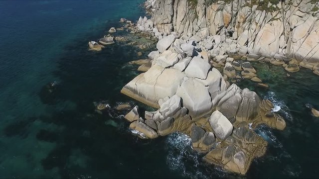 Aerial shot moving along the coastline of deep blue sea along a dramatic cliff edge on sunny day