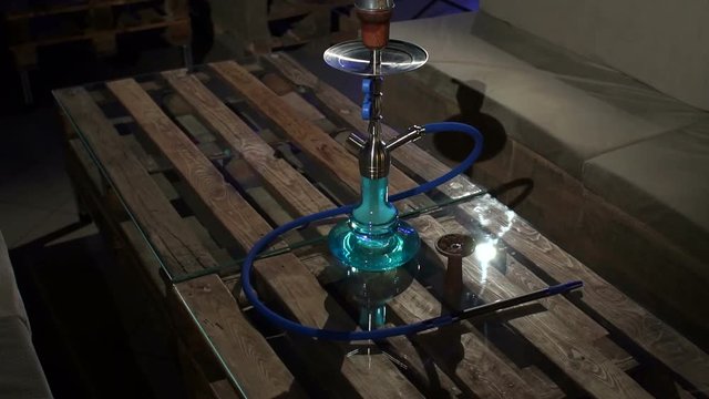 A green glass hookah with tubes and fruit tobacco stands on a table made of pallets in the lounge bar. Stylish oriental shisha. Shisha Smoking Concept. Slow motion.