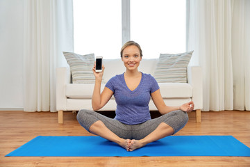 fitness, technology and healthy lifestyle concept - woman with smartphone doing yoga at home