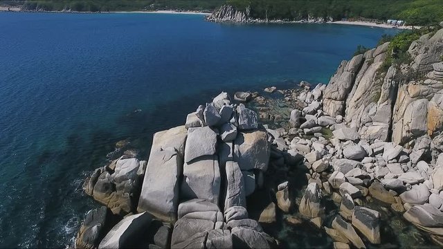 Aerial shot moving along the coastline of deep blue sea along a dramatic cliff edge on sunny day