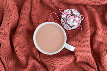 Cup of coffee with milk and chocolate cookies on warm knitted coral blanket.