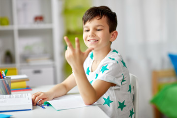 education, childhood and school concept - happy student boy counting using fingers at home