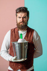 Waiter holds wine cooler with bottle of champagne. Waiter man. Bottle of wine in bucket with ice. Waiter in high class restaurant. Butler with ice bucket with champagne bottle.