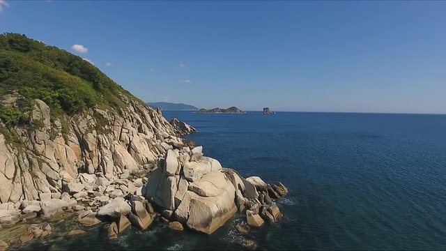 Aerial shot moving along the coastline of deep blue sea along a dramatic cliff edge on sunny day