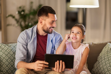 family, fatherhood and technology concept - happy father and little daughter with tablet pc computer and earphones listening to music at home