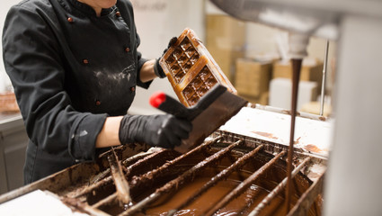 production, cooking and people concept - confectioner cleaning mold from extra chocolate by spatula...