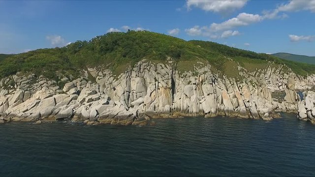 Aerial shot moving along the coastline of deep blue sea along a dramatic cliff edge on sunny day