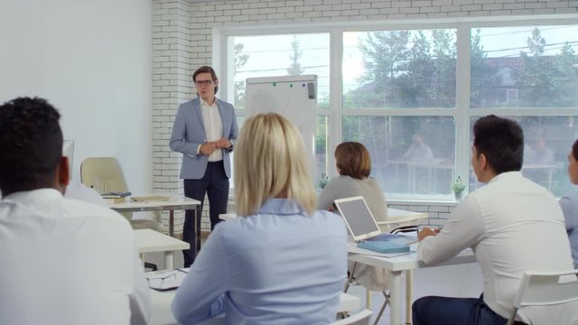 Male business coachee standing by flipchart, drawing graph and explaining it to group of employees in seminar room