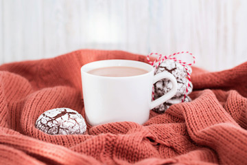 Cup of coffee with milk and chocolate cookies on warm knitted coral blanket.