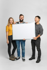 Portrait of three funny laughing young people wearing casual clothes, holding mockup white board isolated in studio, white background