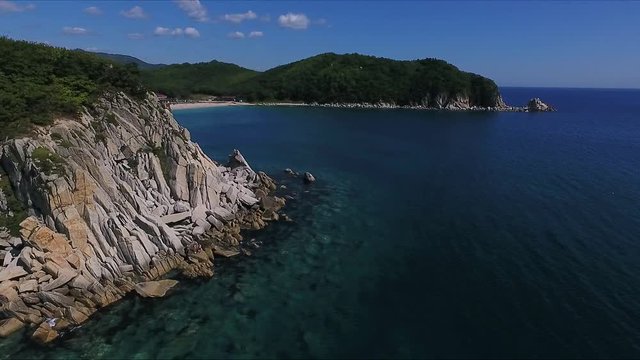 Aerial shot moving along the coastline of deep blue sea along a dramatic cliff edge on sunny day