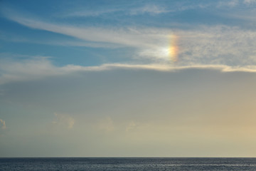 Blue cloudy sky with rainbow effect over the sea on a sunset as a natural background.