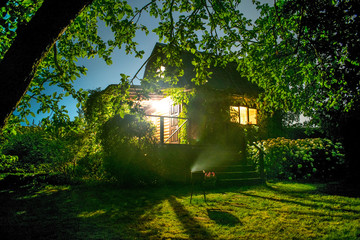 Wooden House with lights in the garden with green trees