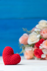Valentines day concept. hand make yarn red heart in front of rose flower bouquet on wooden table and blue background