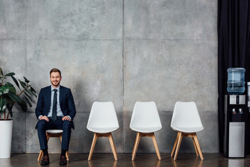 stylish businessman in suit sitting in waiting hall and looking at camera