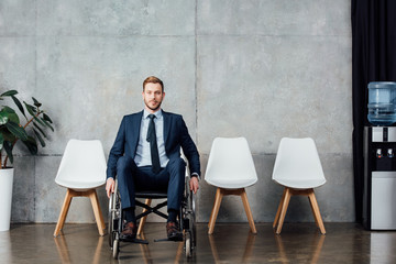 stylish businessman sitting in wheelchair in waiting hall and looking at camera