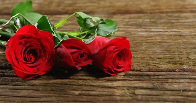 Three red roses on wooden surface 4k