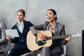 multiethnic businesswomen playing guitar and using digital tablet in office
