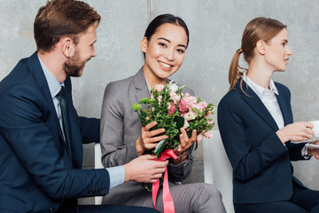 businessman presenting flowers to beautiful smiling asian businesswoman in office