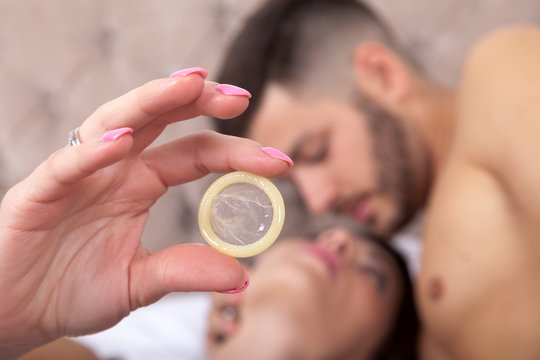 woman's hand holding a transparent condom while a passionate moment in bed with her partner