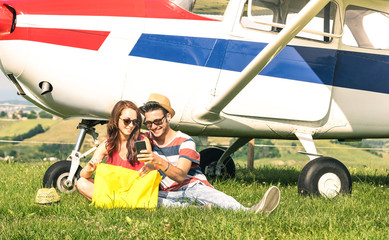 Young couple of lovers having a rest during charter airplane excursion - Wanderlust concept of alternative people lifestyle traveling around the world - Love and fun sharing images on mobile phone