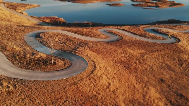 Electric Skateboarding Downhill on Upper Section of Curvy Path with Switchbacks at Golden Hour Aerial View