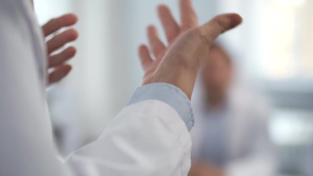 Close-up shot of hands of practitioner in lab coat explaining something to audience during medical seminar; foreground focus