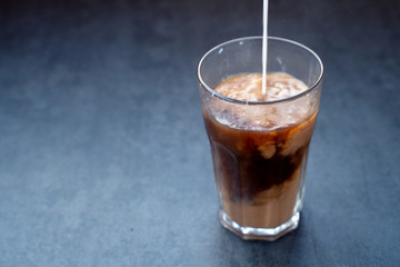 Pouring milk into coffee latte in the glass on a dark gray stone table, copy space.