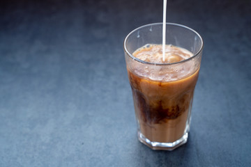 Pouring milk into coffee latte in the glass on a dark gray stone table, copy space.