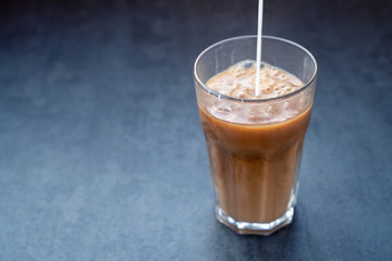 Pouring milk into coffee latte in the glass on a dark gray stone table, copy space.