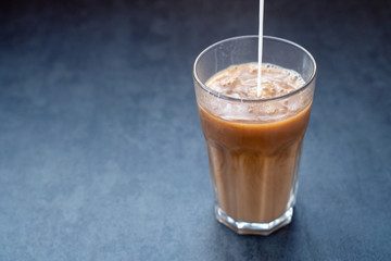 Pouring milk into coffee latte in the glass on a dark gray stone table, copy space.