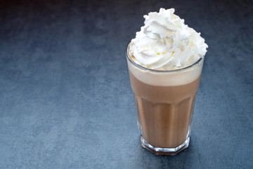 Cold hot coffee drink latte, with whipped in glass cream on a dark gray stone table, copy space.