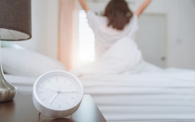Woman stretching in bed after waking up, back view. Woman sitting near the big white window while...