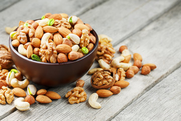 Wooden bowl with mixed nuts on a wooden gray background. Walnut, pistachios, almonds, hazelnuts and cashews, walnut.