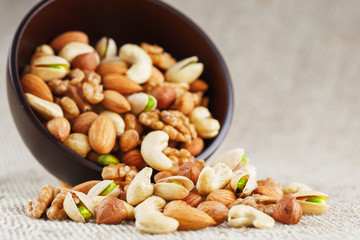 Mix of different nuts in a wooden cup against the background of fabric from burlap. Nuts as structure and background, macro. Top view.