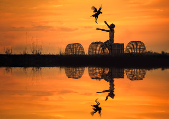 Fototapeta na wymiar Silhouettes of men and chicken in the beautiful sunset with reflection water,life style in Thailand.
