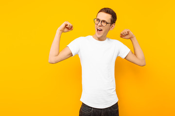 Fototapeta premium man in glasses, dressed in a white T-shirt, the man who won shows a gesture of victory and success, on a yellow background