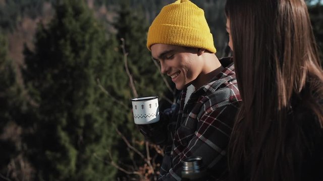 Couple in love drink tea from a mug of thermos on the background of mountains. Tourists sitting on stones and looking on beautiful nature. Tourism, rest, vacation, nature, hike concept