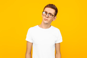 Handsome man in glasses, dressed in a white T-shirt, posing on a yellow background