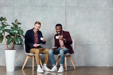 multiethnic men sitting, looking at camera and drinking coffee in waiting hall