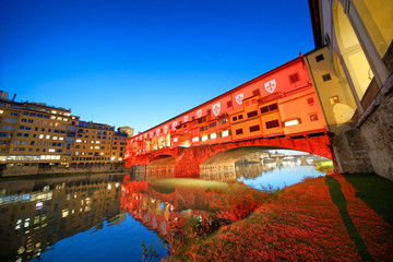 Old Bridge in Florence at night with Arno River reflections and red right projected on the landmark