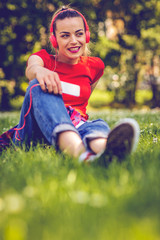 Fototapeta premium happy woman with earphones and smartphone listening to music on grass.